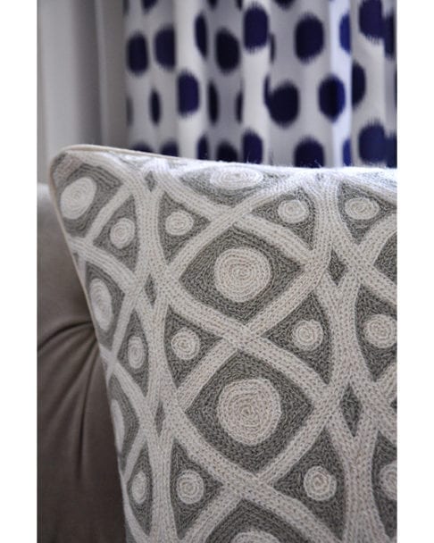 Grey crewelwork cushions detail shot with grey sofa and a blue spotted curtain behind.