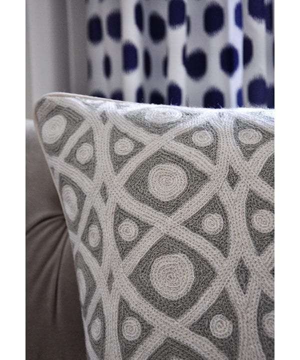 Grey crewelwork cushions detail shot with grey sofa and a blue spotted curtain behind.