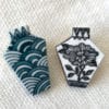 Two porcelain Japanese jewellery brooches depicting a monochrome floral design and a repeating Japanese waves motif - a symbol of tranquility.