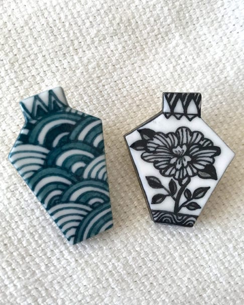 Two porcelain Japanese jewellery brooches depicting a monochrome floral design and a repeating Japanese waves motif - a symbol of tranquility.