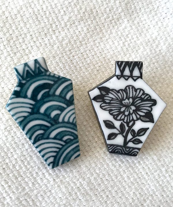 Two porcelain Japanese jewellery brooches depicting a monochrome floral design and a repeating Japanese waves motif - a symbol of tranquility.