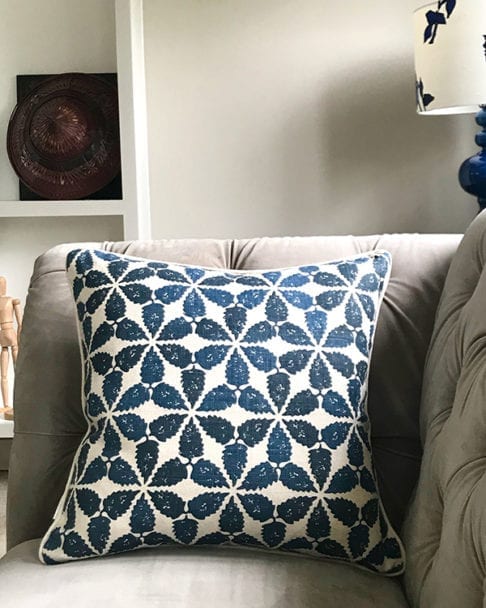 An indigo patterned cushion with a Moroccan motif on a grey, velvet Chesterfield sofa.