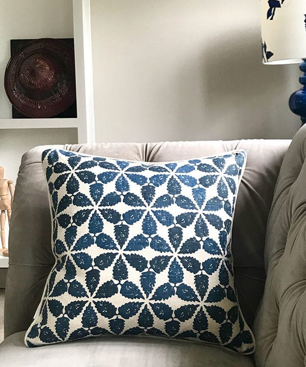 An indigo patterned cushion with a Moroccan motif on a grey, velvet Chesterfield sofa.