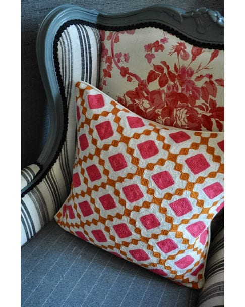 A pink and orange, diamond design crewel-work cushion on a French-style armchair.