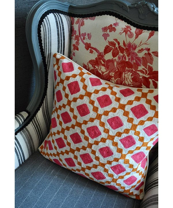 A pink and orange, diamond design crewel-work cushion on a French-style armchair.