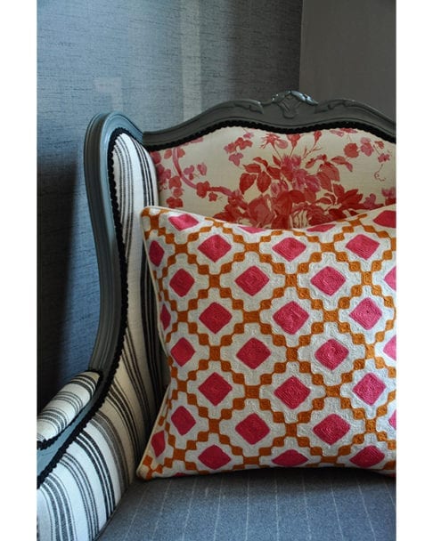 A pink and orange, diamond design crewel-work cushion on a French armchair.