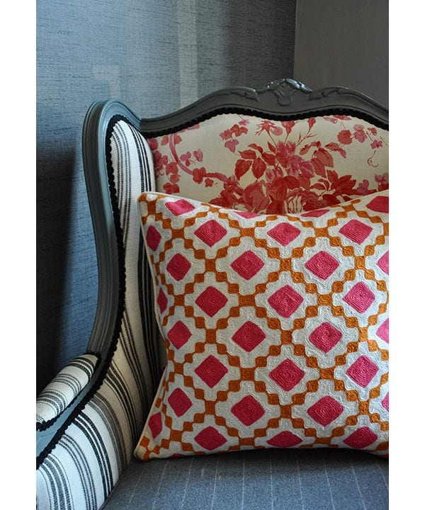 A pink and orange, diamond design crewel-work cushion on a French armchair.