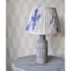 Indigo blue gathered silk lampshades in Japanese-style Shibori silk. The lampshade is sat on a painted, grey, side table with geometric wallpaper behind.