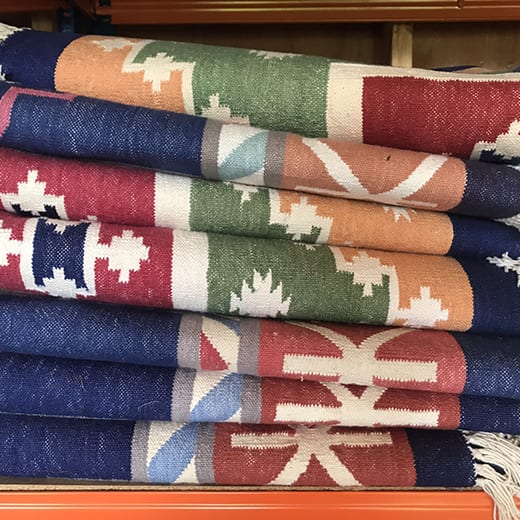 A pile of vibrantly-coloured tasselled kilims in blue, red, orange and green.