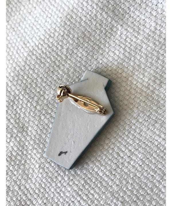 The back of the porcelain jewellery brooches with a gold-coloured pin and the artist's signature.