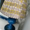 Lampshades in chartreuse and putty, block-printed in India on cotton voile, displayed here on a blue ceramic lamp base.