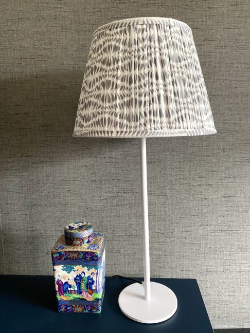 Grey patterned lampshades in. various sizes, hand block-printed in India. Styled here against a darker grey backdrop with a vintage Chinese ceramic pot.