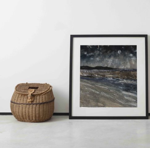 Irish wall art print Five Finger Strand is leaned against a wall next to an old-fashioned wicker picnic basket.