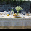 Yellow linen tablecloth with subtle motifs that reference Hungarian folk patterns. Draped over a table outside, set with glasses and tableware.