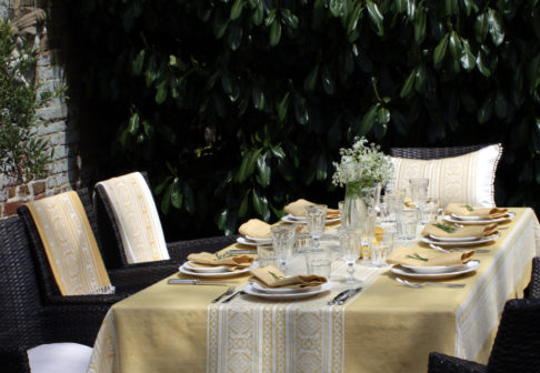 An outdoor table set for supper with a soft yellow tablecloth depicting jacquard-woven, Hungarian folk patterns.