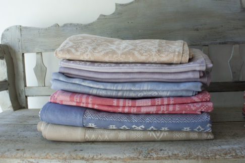 A pile of luxurious, folk-inspired tablecloths in a pretty palette of pastels on an antique bench.