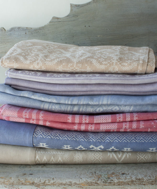 A pile of luxurious, folk-inspired tablecloths in a pretty palette of pastels on an antique bench.