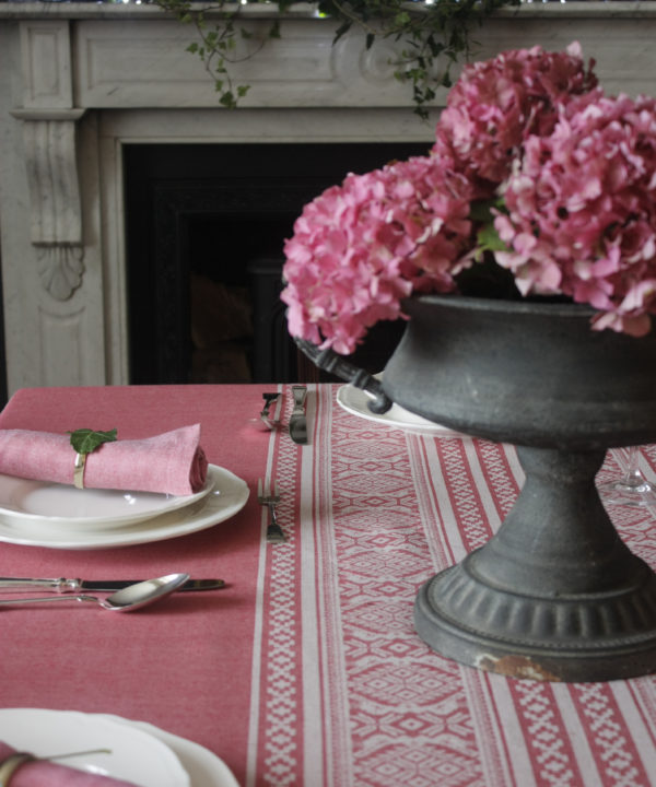 A deep pink Hungarian-folk-inspired tablecloth on a laid table with an urn filled with pink hydrangeas.