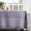 Purple tablecloth made from linen, with a Hungarian folk inspired jacquard weave, draped over a vintage mahogany dining table in front of a window.