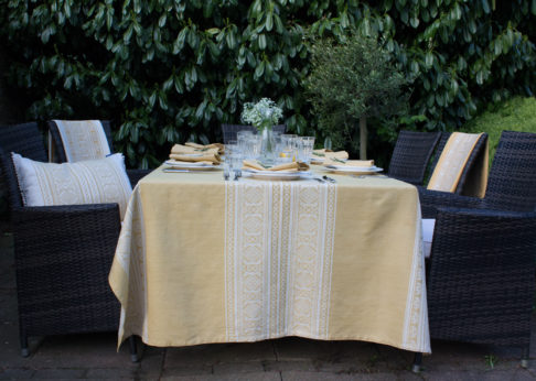 An elegant outdoor table set for supper with a soft yellow tablecloth depicting jacquard-woven, Hungarian folk patterns.