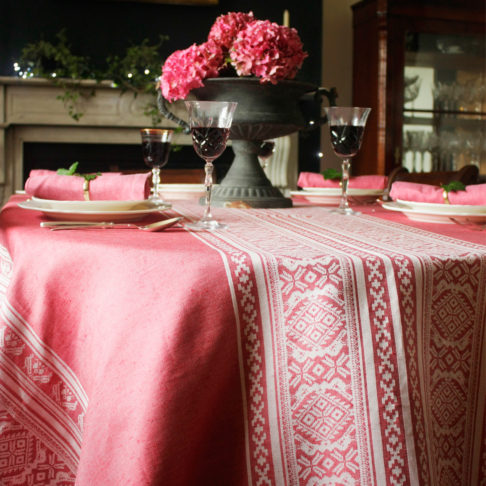 An elegant table, laid for supper and dressed with a deep pink tablecloth depicting Hungarian folk patterns.