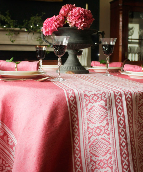 An elegant table, laid for supper and dressed with a deep pink tablecloth depicting Hungarian folk patterns.