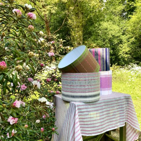 A selection of handmade drum lampshades in pinks and greens styled in a garden setting.