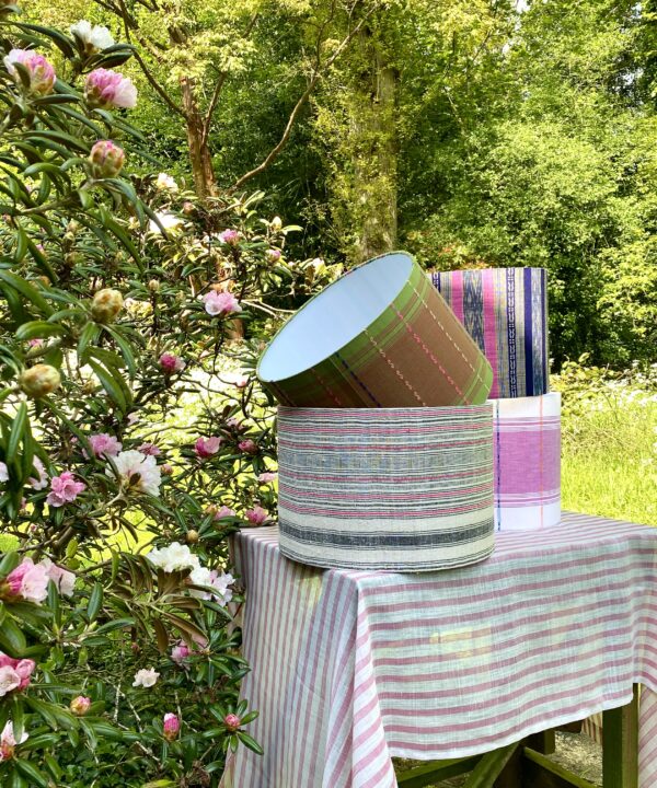 A selection of handmade drum lampshades in pinks and greens styled in a garden setting.