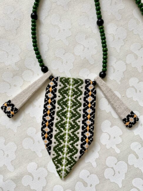 An embroidered textile necklace in green and black.