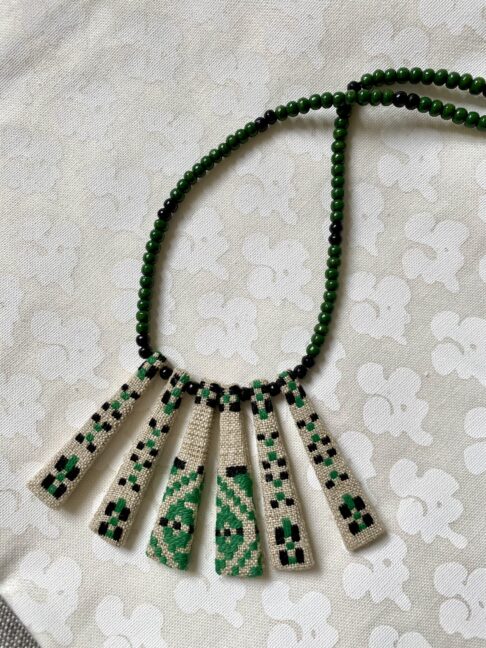 A green bib necklace with a beaded chain showcasing a vintage Slovenian embroidered textile.