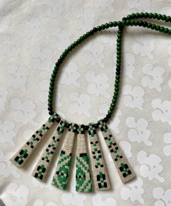 A green bib necklace with a beaded chain showcasing a vintage Slovenian embroidered textile.