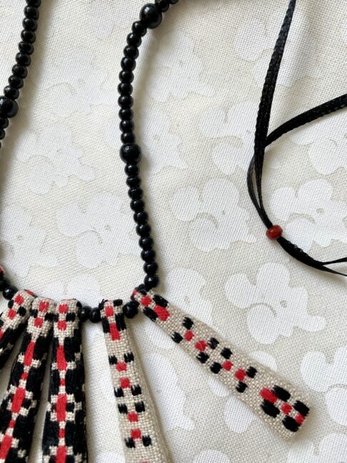 Detail of a pretty, Boho-style necklace in red and black with beaded ribbon and vintage embroidered textile.