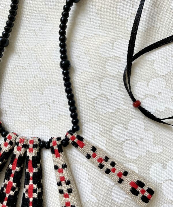 Detail of a pretty, Boho-style necklace in red and black with beaded ribbon and vintage embroidered textile.