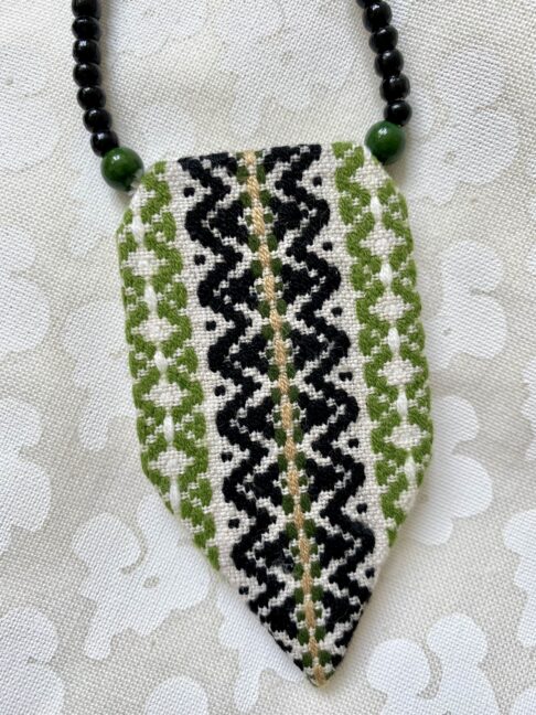 A chic, embroidered panel necklace with a beaded ribbon fastening.