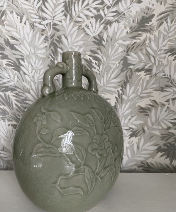 An ovoid, celadon pottery pot handmade in Thailand displayed against soft grey-green yew tree wallpaper.