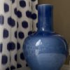 A decorative blue pot, largescale, against blue polka dot curtain fabric.