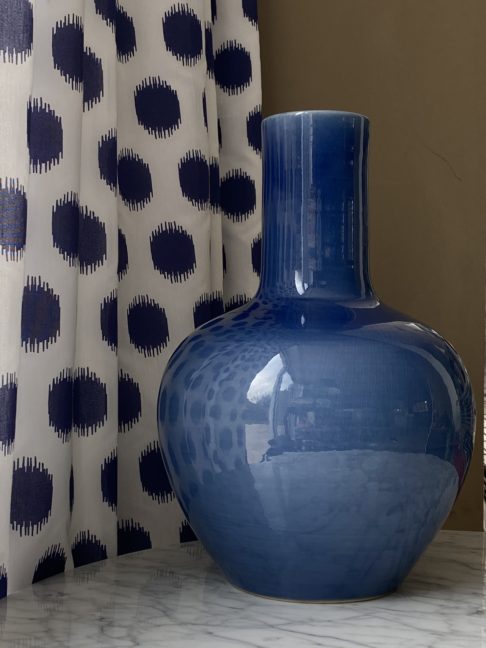 A decorative blue pot, largescale, against blue polka dot curtain fabric.