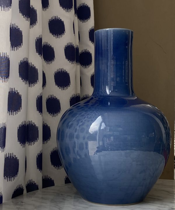 A decorative blue pot, largescale, against blue polka dot curtain fabric.