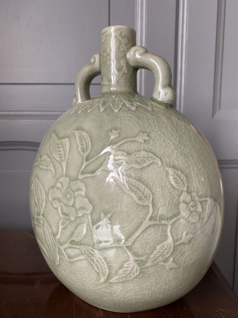 An elegant, hand-decorated celadon pot against a panelled grey backdrop.