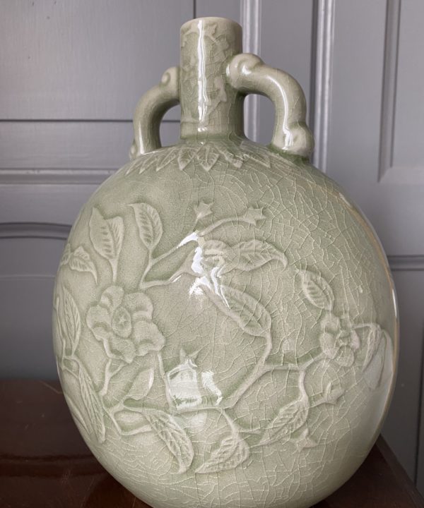 An elegant, hand-decorated celadon pot against a panelled grey backdrop.