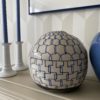 Geometric pottery pot in blue and cream on a beige bookshelf with white candlesticks behind.