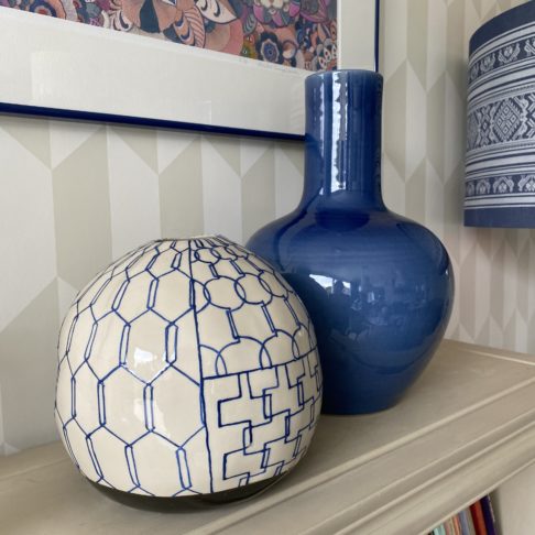 Two blue, Asian-style, ceramic pots on a bookshelf with subtle geometric wallpaper in the background.