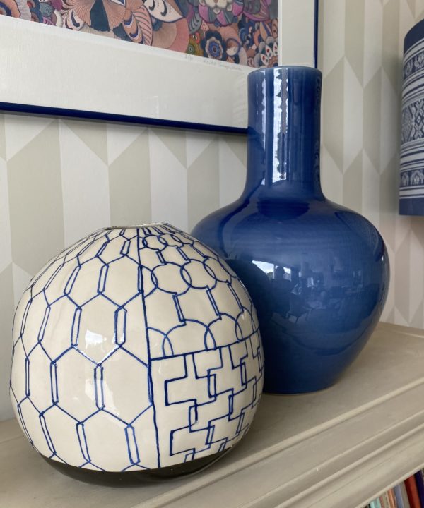 Two blue, Asian-style, ceramic pots on a bookshelf with subtle geometric wallpaper in the background.