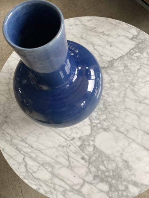 An overhead view of a large, Asian style pot in blue, on a white marble coffee table.