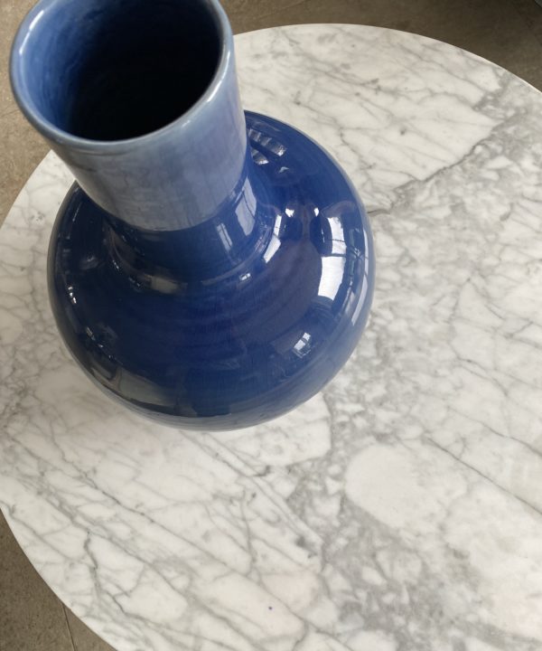 An overhead view of a large, Asian style pot in blue, on a white marble coffee table.