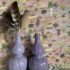 Purple ceramic pot, handmade in Thailand, double-gourd-shaped and shown holding feathers against a pretty, pastel, Aboriginal art wallpaper.