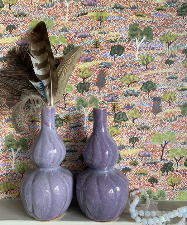 Purple ceramic pot, handmade in Thailand, double-gourd-shaped and shown holding feathers against a pretty, pastel, Aboriginal art wallpaper.