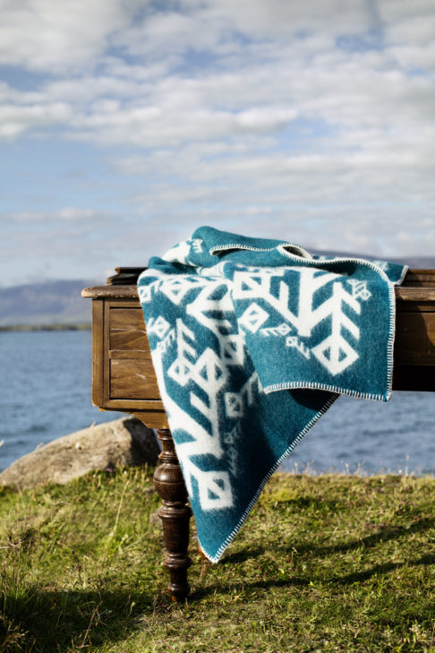 A turquoise bind rune motif blanket styled on a table in the Icelandic outdoors.