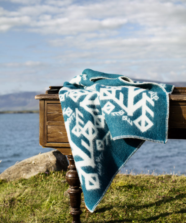 A turquoise bind rune motif blanket styled on a table in the Icelandic outdoors.