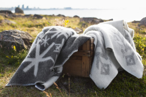 Bind rune blankets in pale and dark greys styled on a wooden crate with the Icelandic countryside as a backdrop.